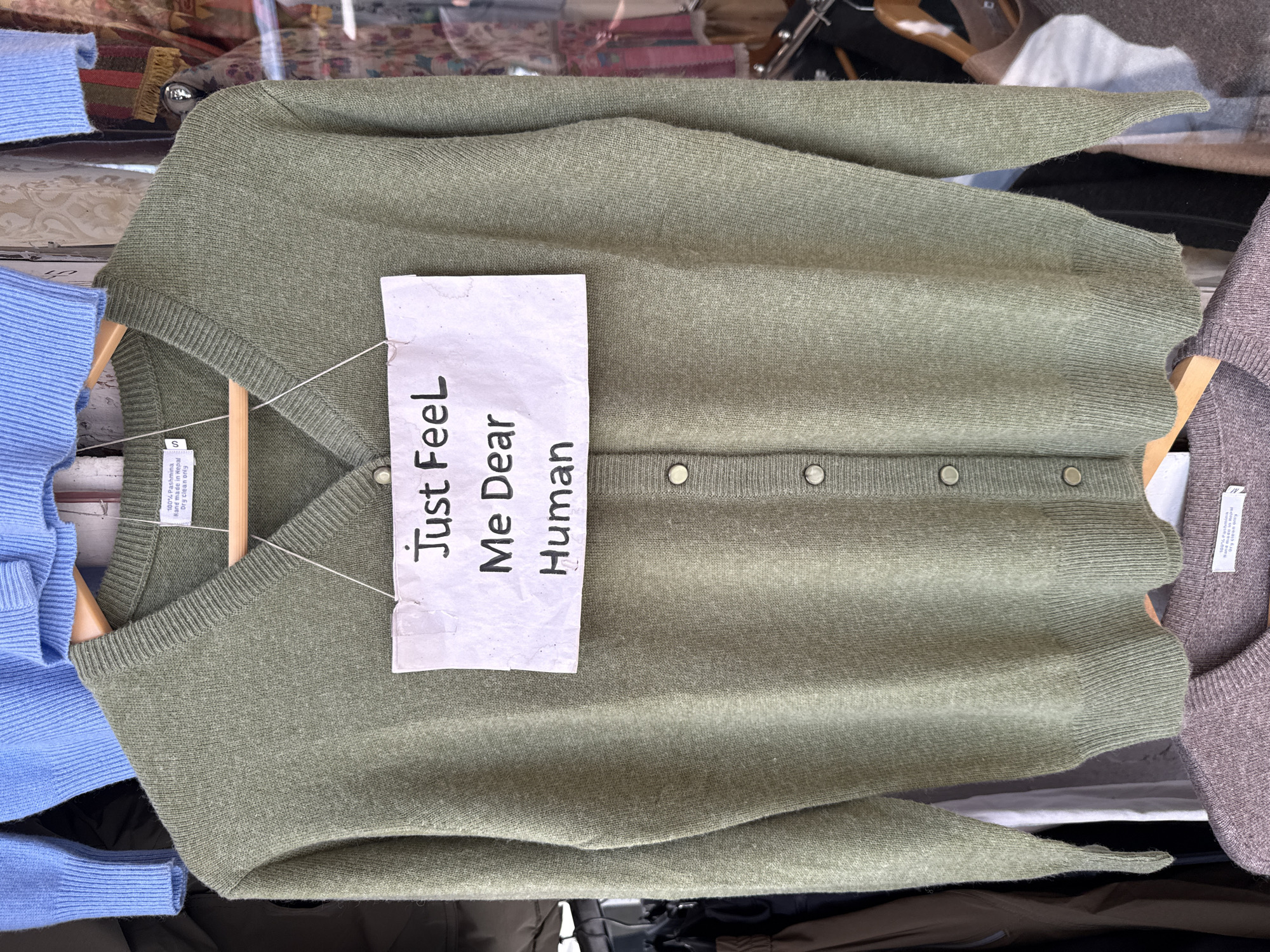Green cardigan with handwritten note displayed in Pokhara shop