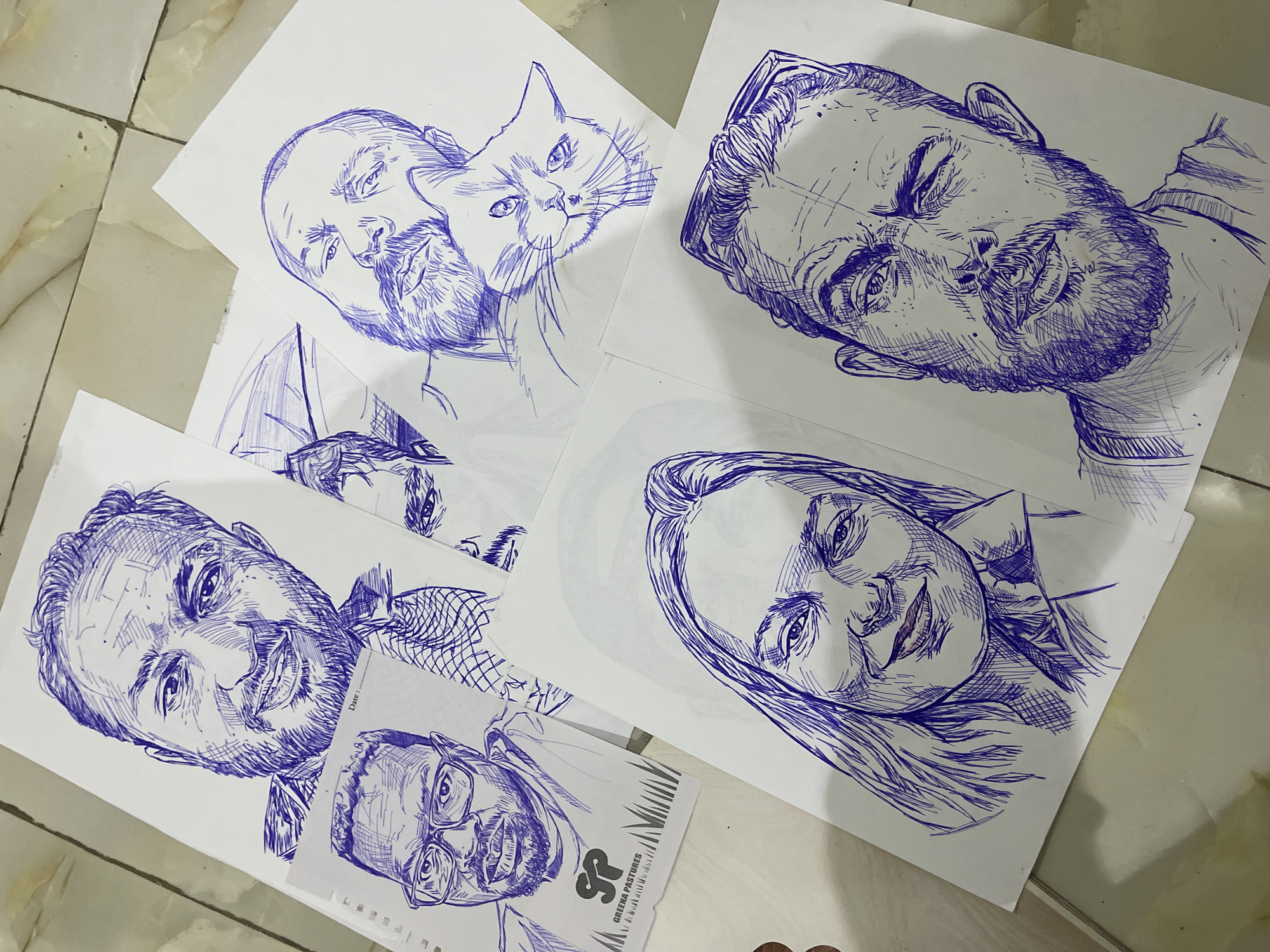 Blue ink portraits and sketches spread across a floor in Abuja