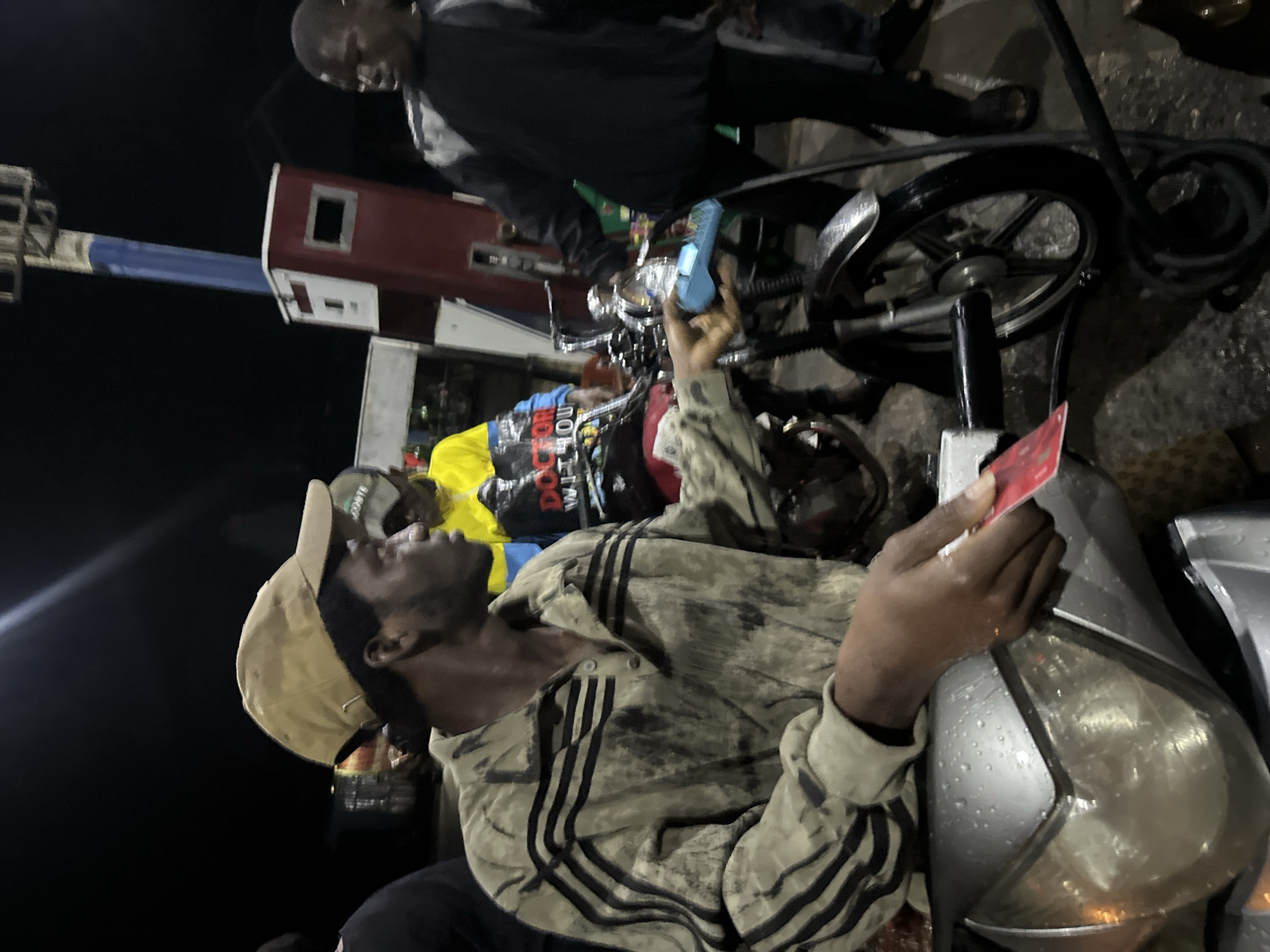 Man with red card sits on motorcycle at Nigerian gas station