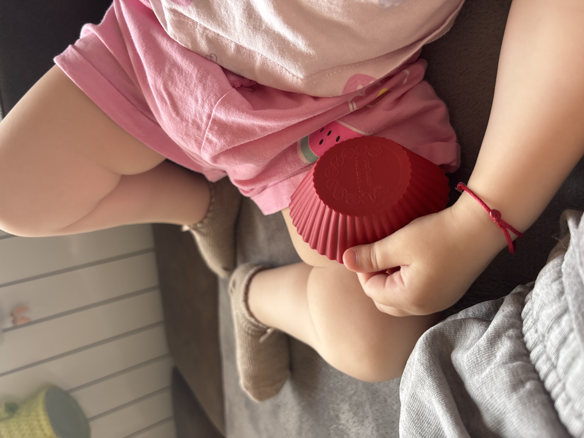 Child with red bracelet and silver ring plays with cupcake liner