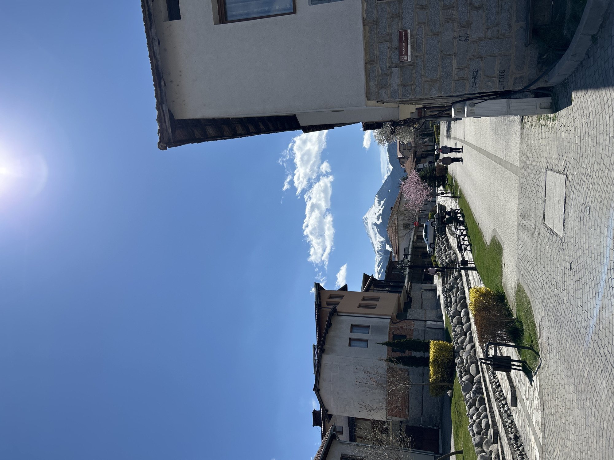 Pedestrians stroll through sunny Bansko with mountain backdrop