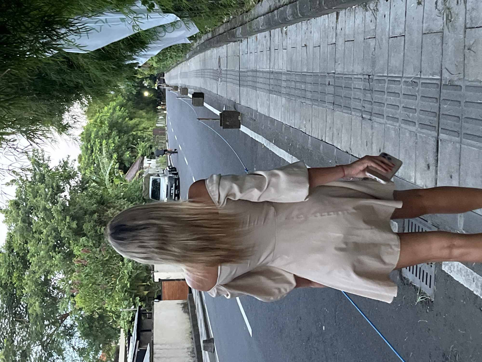 Woman walks Indonesian street amid tropical greenery, passing truck