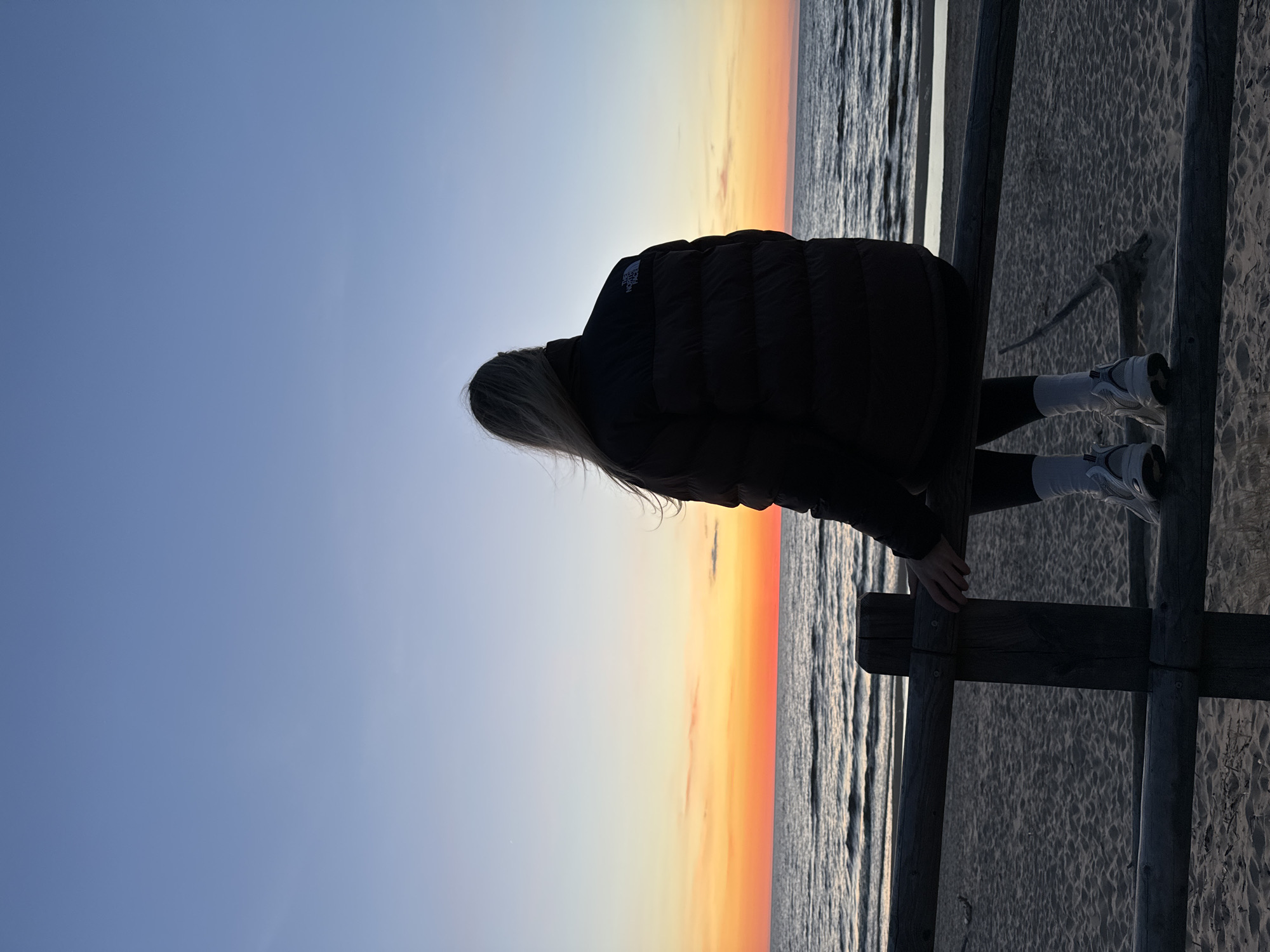 Woman stands on wooden fence overlooking beach in Kalngale