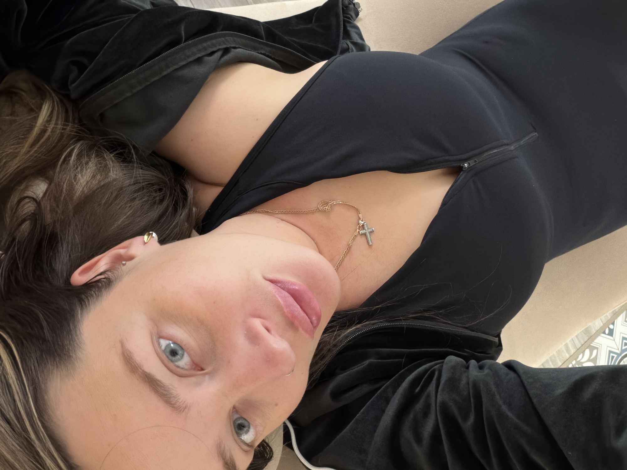 Woman in black outfit observed lying down, wearing cross necklace