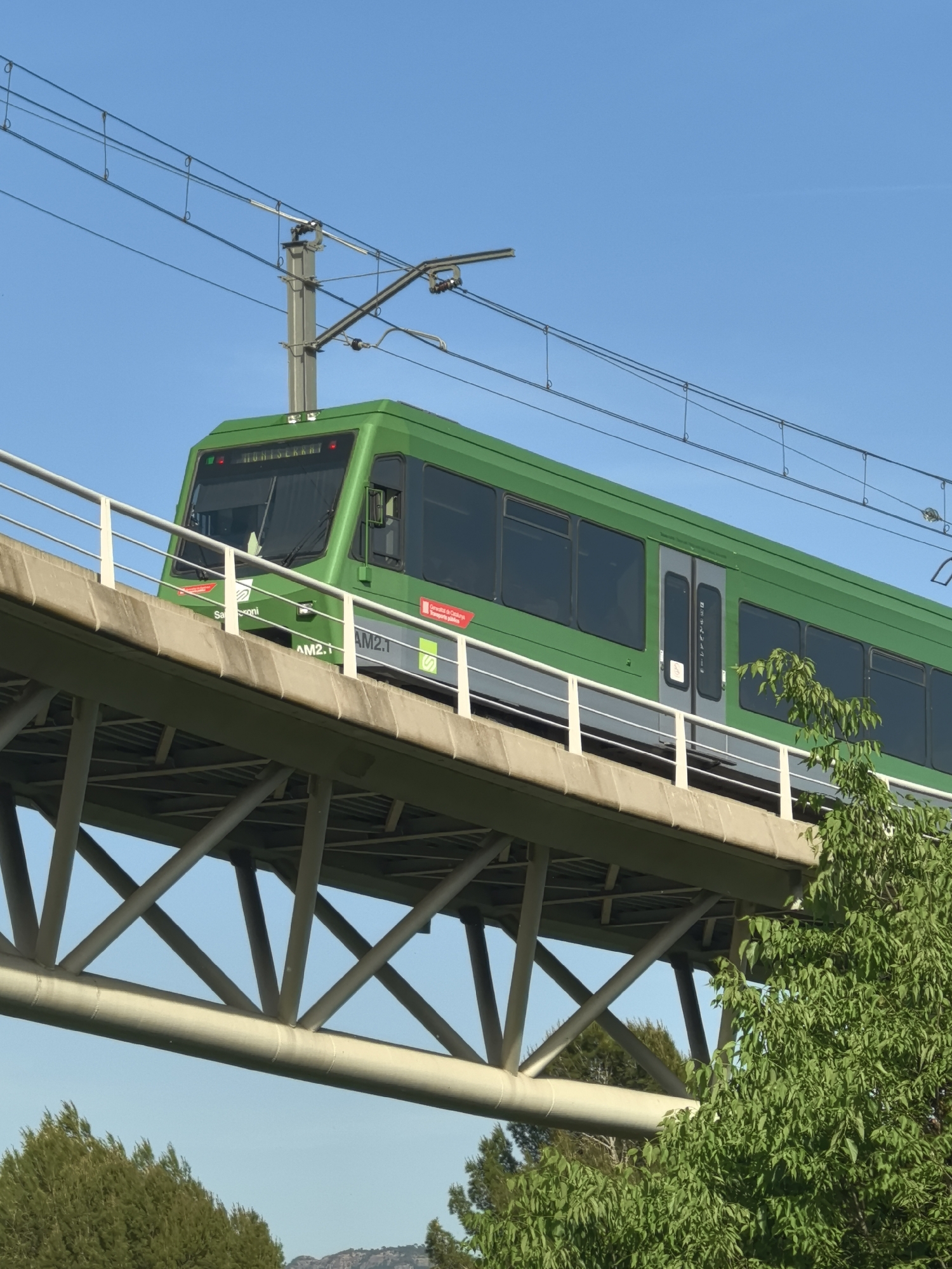 Green electric train crosses elevated bridge in Monistrol de Montserrat