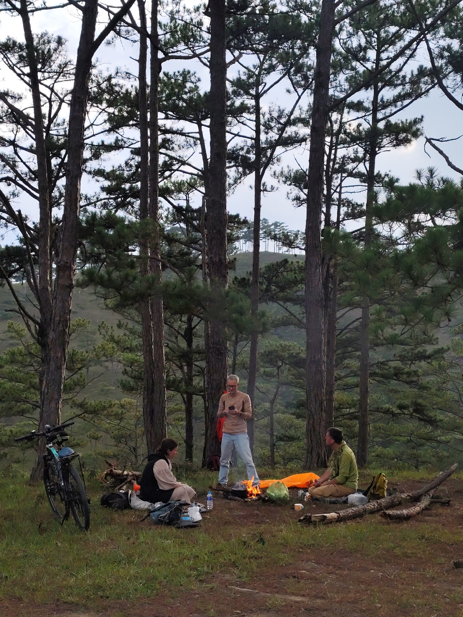 Three campers gather around fire in Vietnamese pine forest