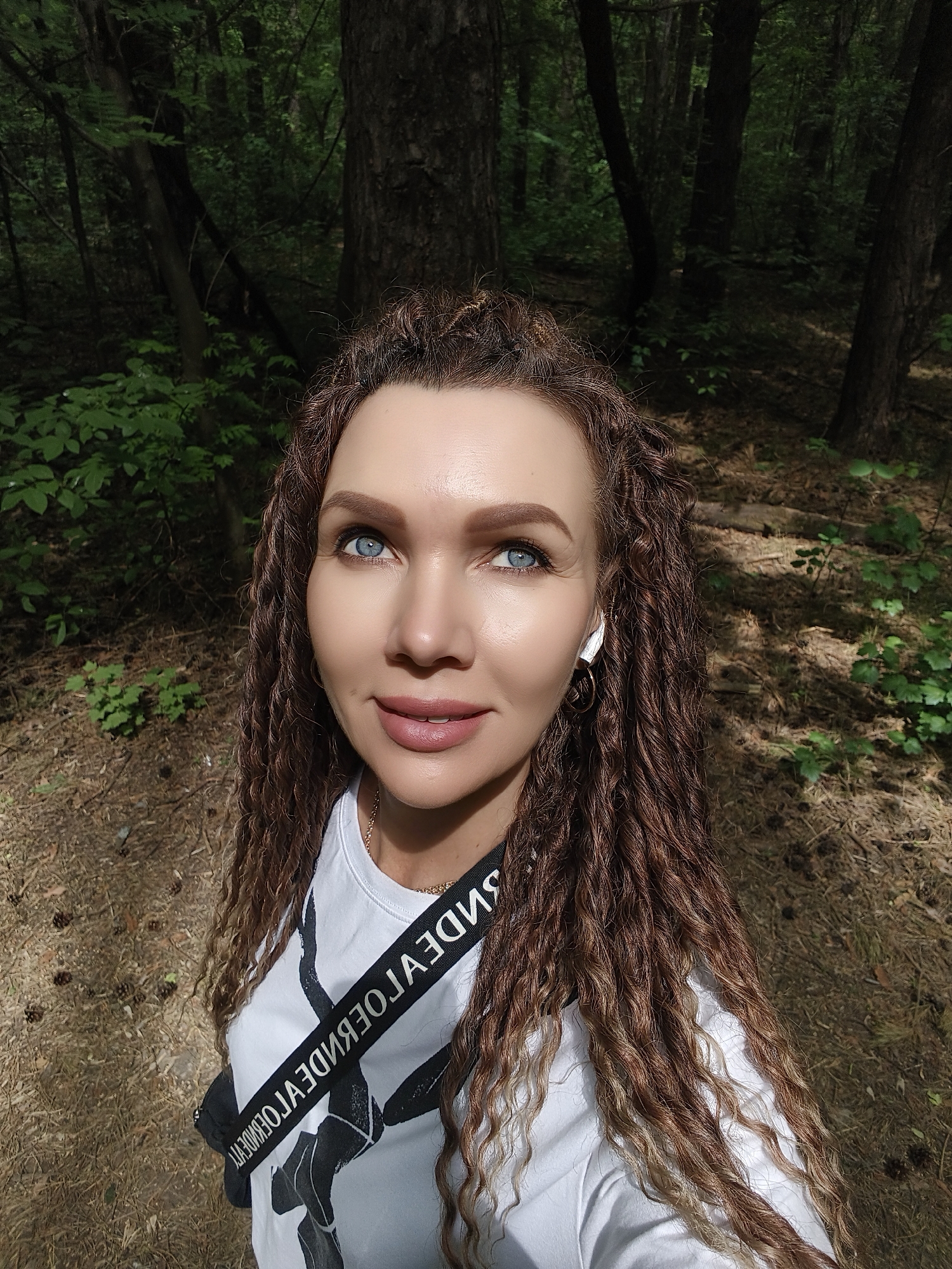 Woman photographing in forest, white shirt, earbuds observed
