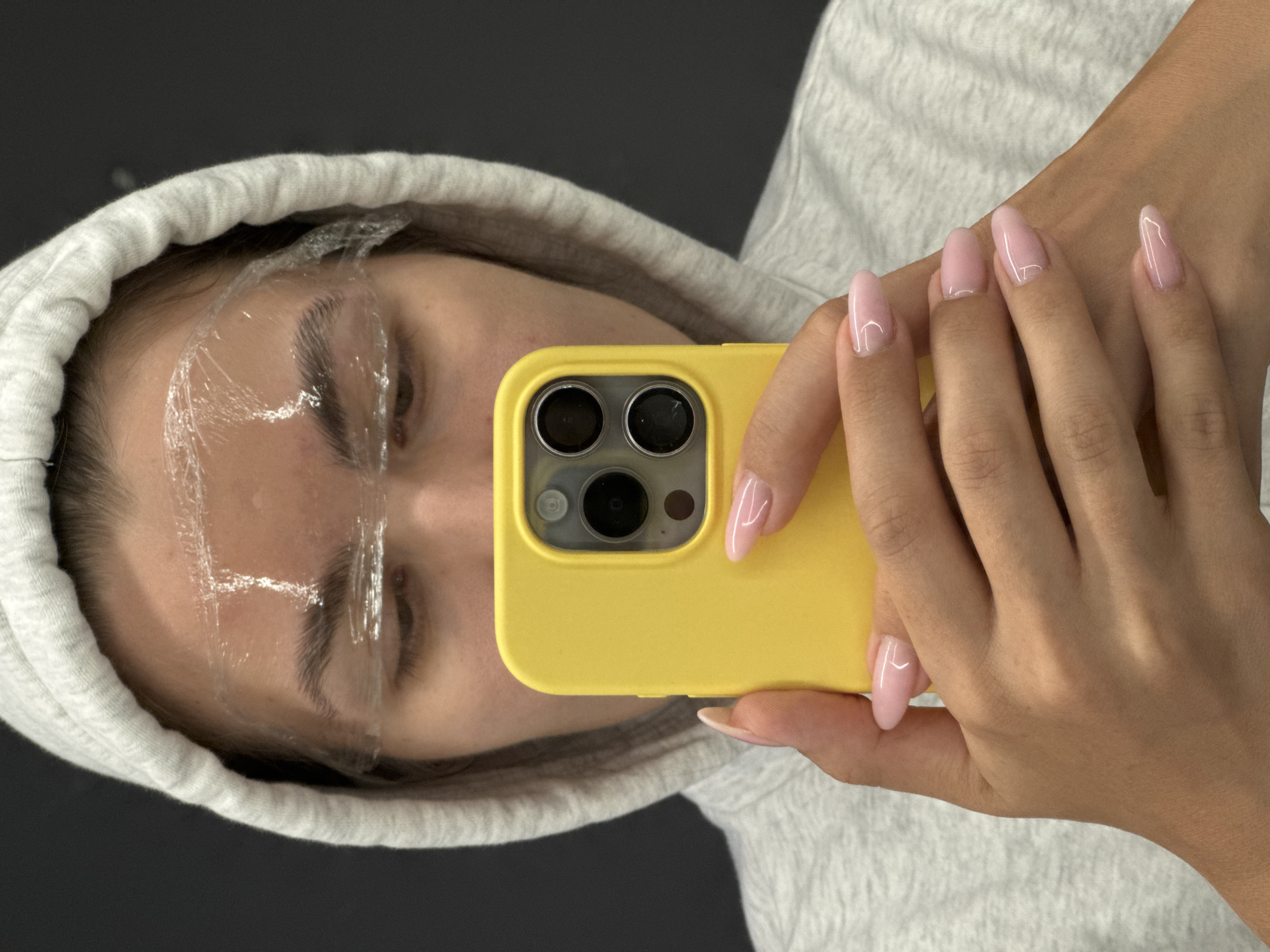 Person takes mirror selfie with yellow phone in gray hoodie