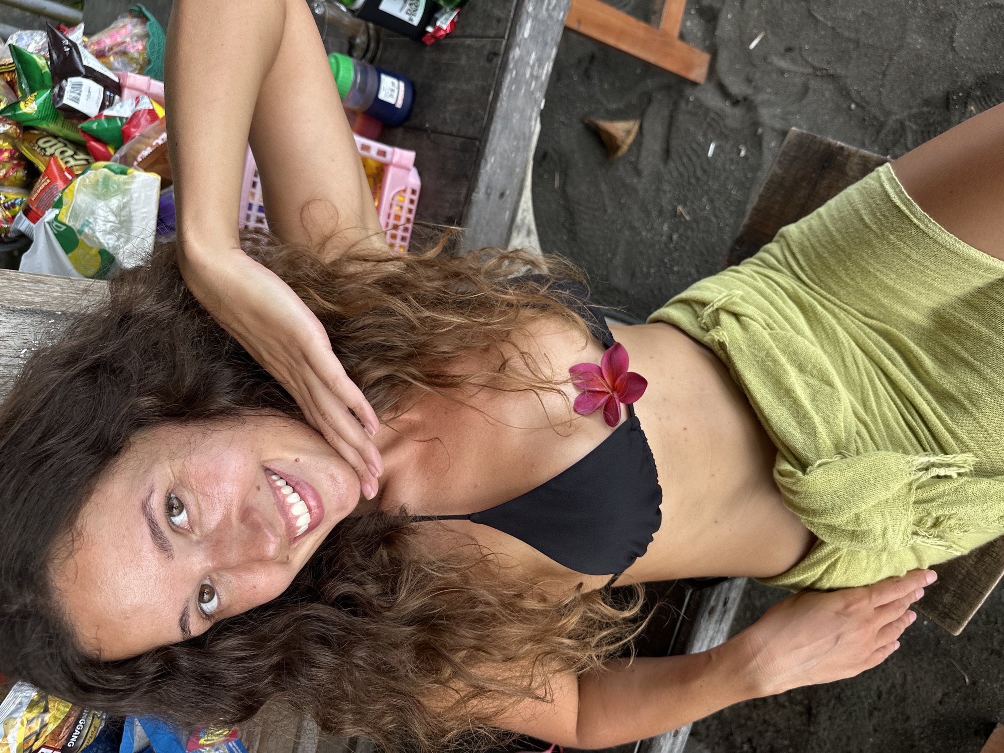 Woman rests with plumeria flowers on wooden surface in Pekutatan