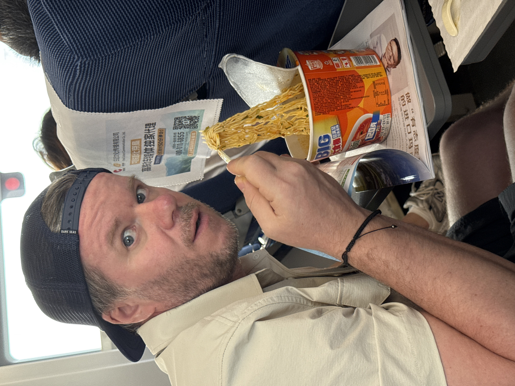 Surprised mid-bite with instant noodles on a flight over China