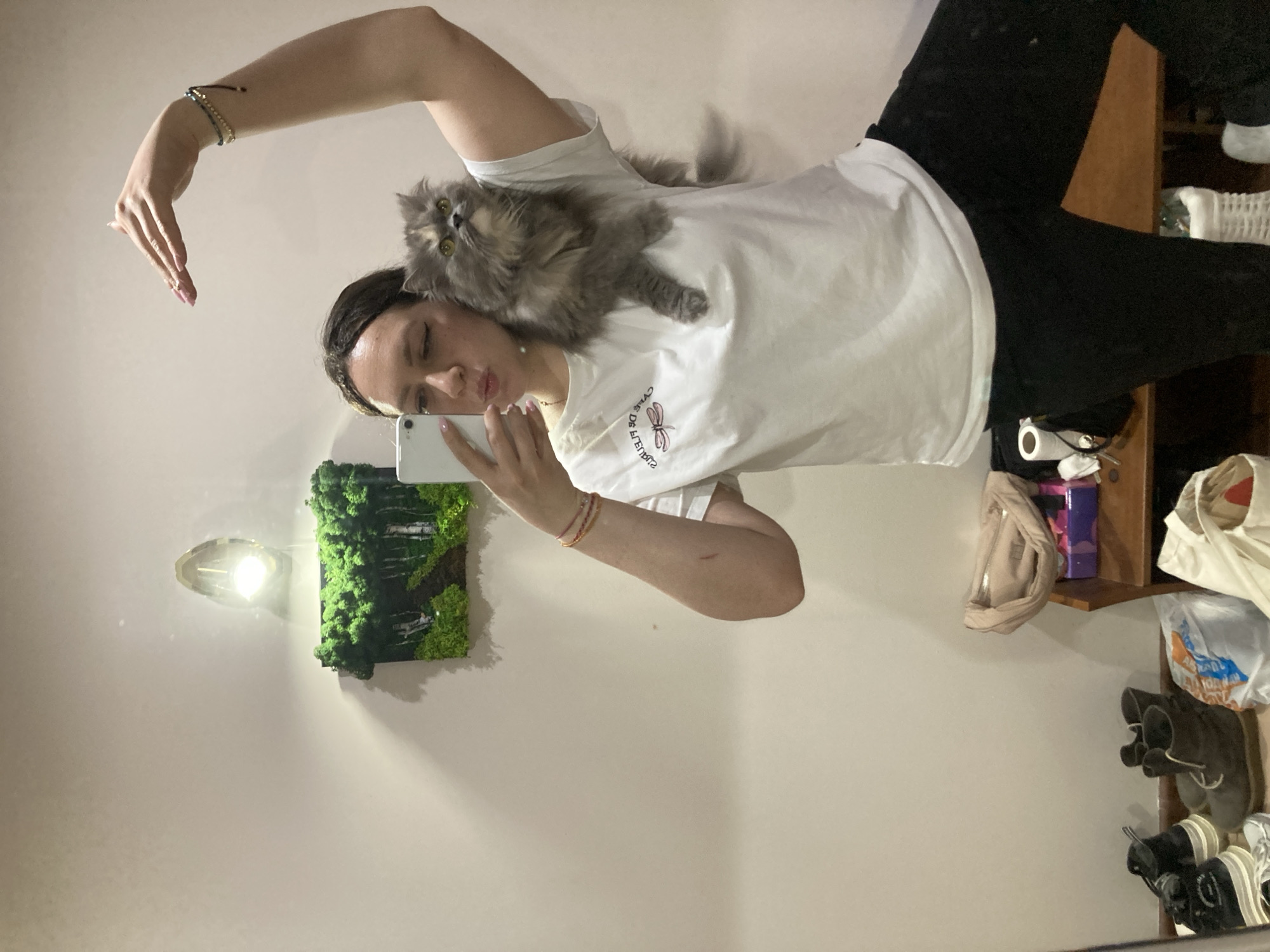 Woman takes selfie with gray cat on shoulder indoors