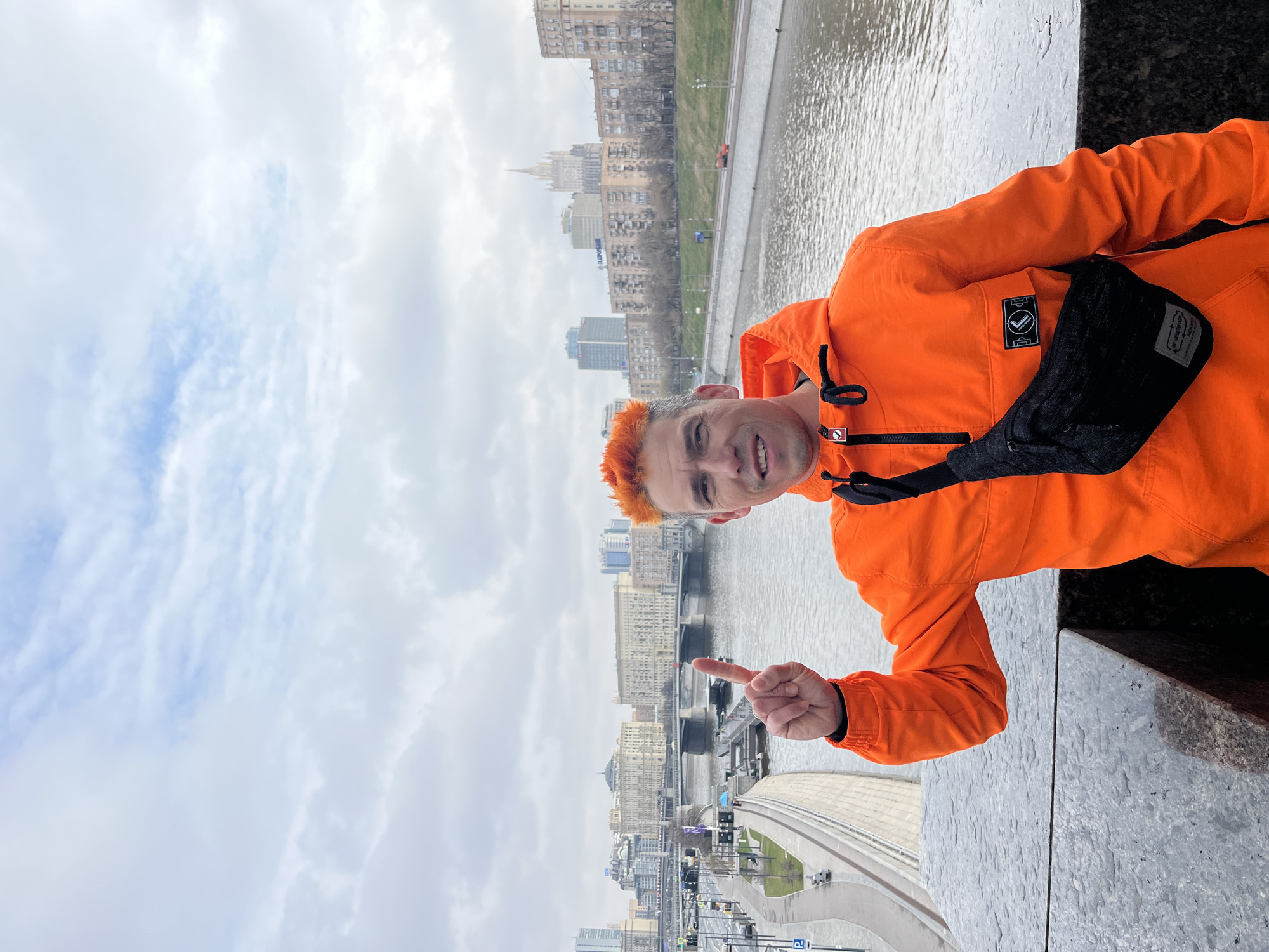 Man in orange jacket observed on platform overlooking city river