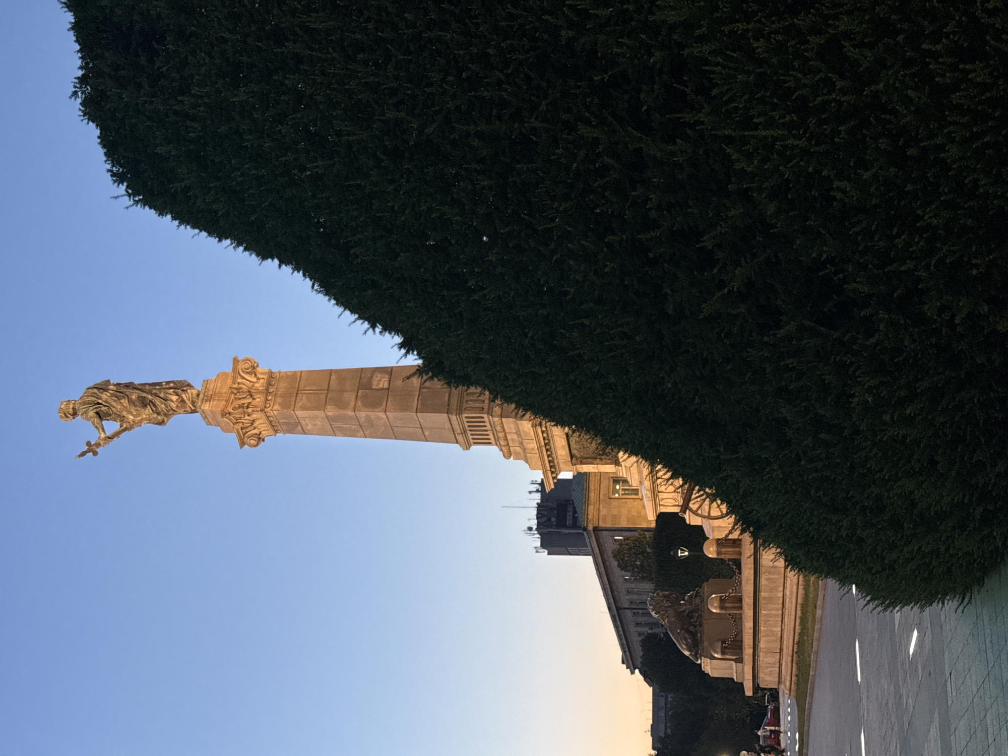 Sword-bearing monument outside a Cyrillic-inscribed civic building at dusk