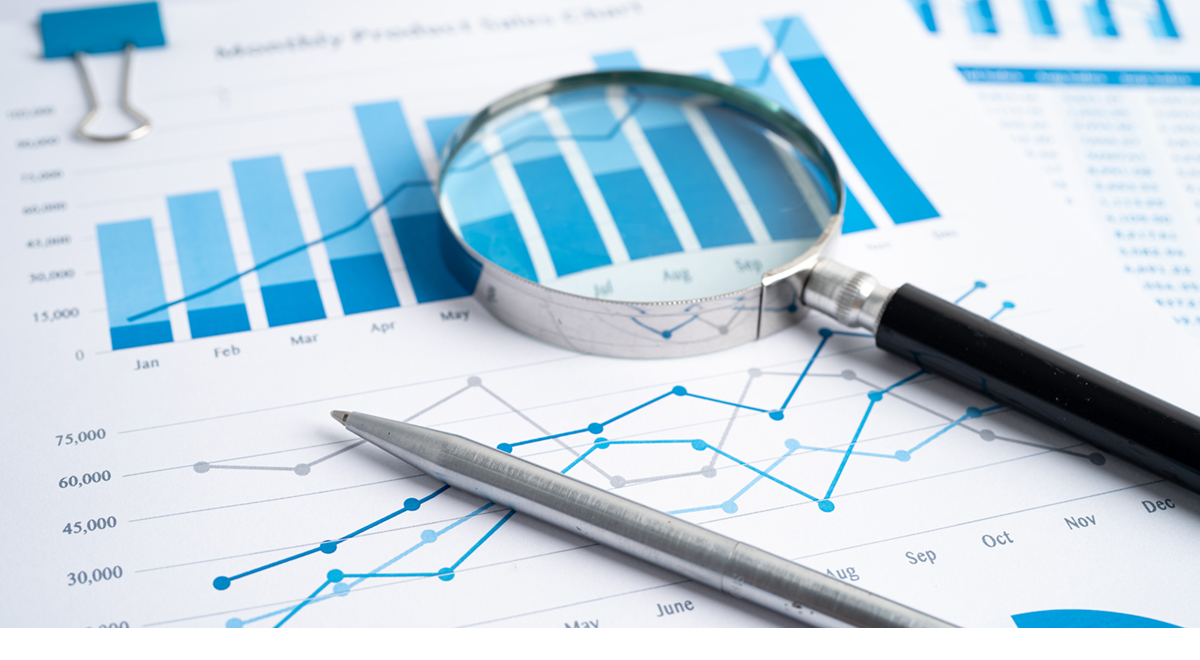 A magnifying glass and pen sit on a data summary, which includes bar and line charts of the organization’s performance