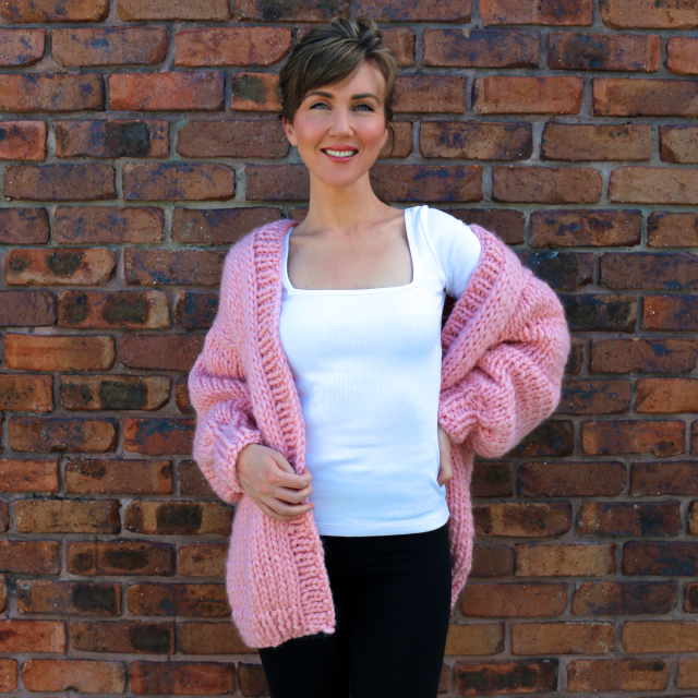 Lisa demonstrating a Pilates exercise in a stylish pink cardigan.