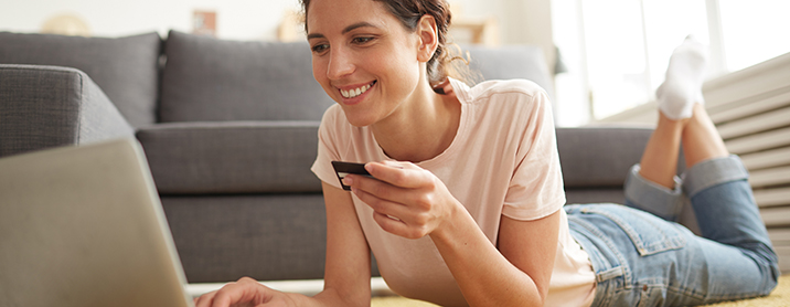 Happy young lady laying in her living room shopping online