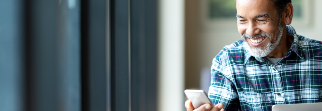 Happy old man browsing the internet on mobile phone and laptop