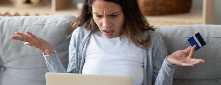 Frustrated young woman holding a credit card in one hand while shrugging and looking at her computer