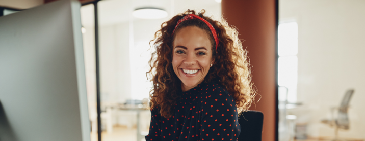 Happy young woman sitting at her computer while smiling at the camera