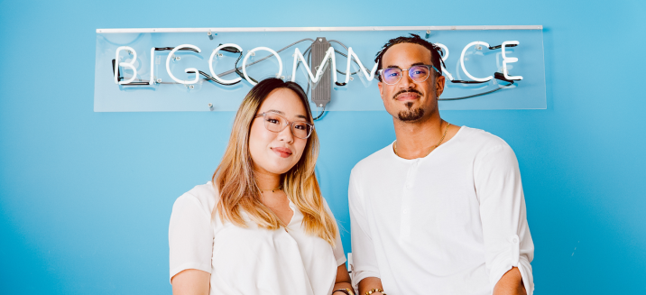 Two BigCommerce employees standing in front of a BigCommerce neon sign