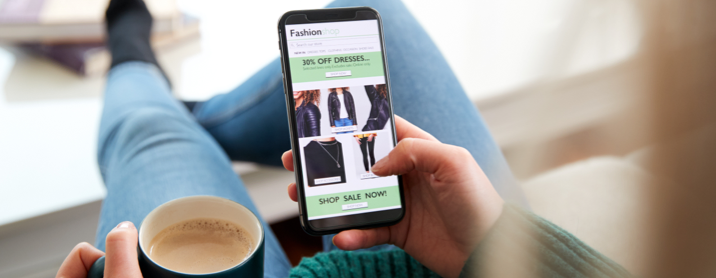 Over the shoulder shot of a woman browsing a mobile eCommerce site while holding a cup of coffee