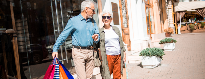 Happy elderly couple walking arm in arm down the street with their shopping bags