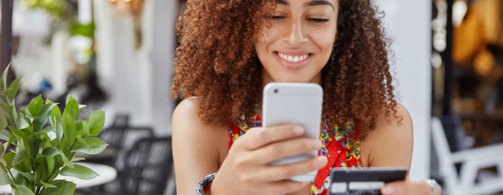 Young curly haired woman sitting outside at a restaurant shopping on her phone