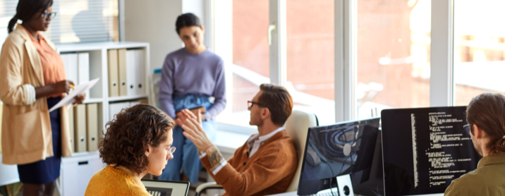 Diverse group of coworkers sitting in an open plan office discussing a project