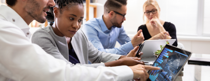 Group of young colleagues sitting at a table reviewing marketing data on tablets