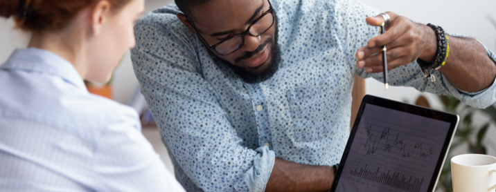 Young man wearing floral button down shirt showing data on iPad to colleague 