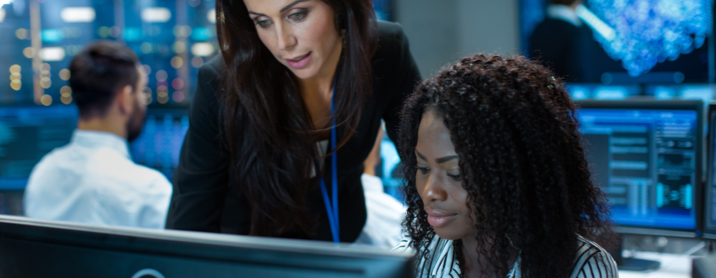 Woman standing behind her employee reviewing data on the employee's computer