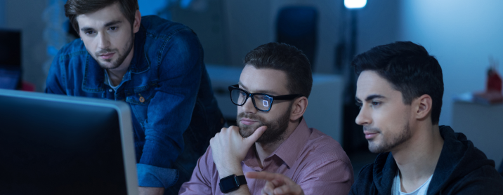 Three young engineers sitting at a computer review code