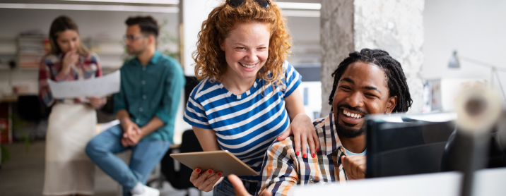 Two colleagues smiling while sitting at a computer