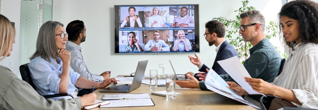 Business team holding meeting in conference room with remote team via video call