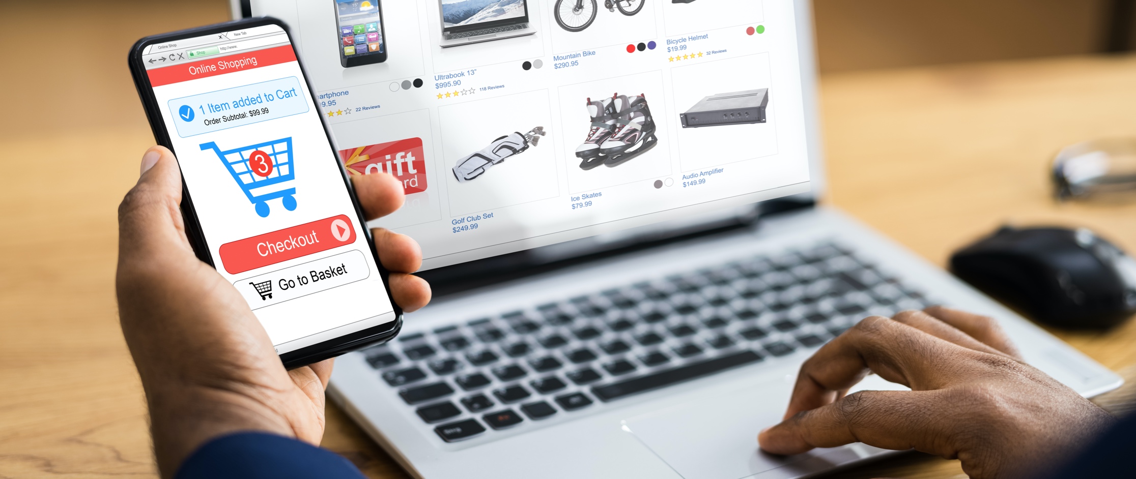 Person holding a cell phone looking at their checkout cart while their laptop is in the background