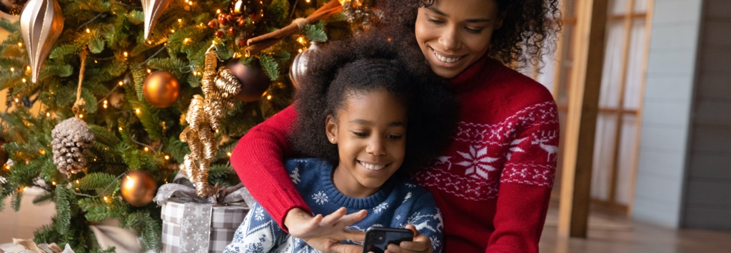 African American mother and daughter using mobile phone in front of Christmas tree