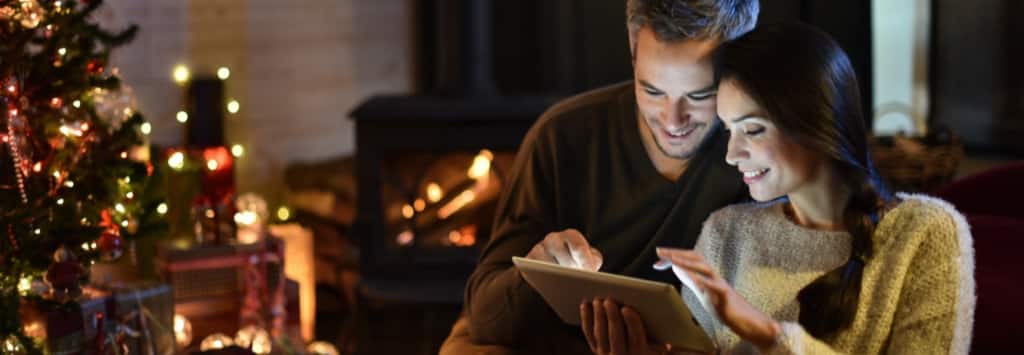 Husband and wife shopping on iPad next to Christmas tree