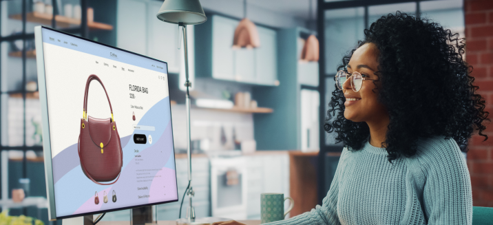 Happy young consumer shopping for purses on her desktop computer