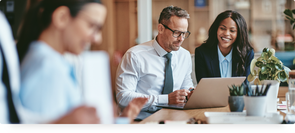 Man dressed in a tie and wearing glasses and woman at a conference table looking at the man's laptop.