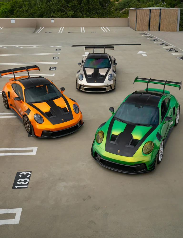 Three Porsche GT3s in orange, silver and green on a parking deck