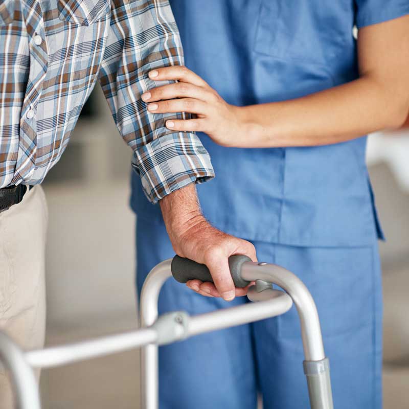 A health care professional helps an elderly man walk with his walker