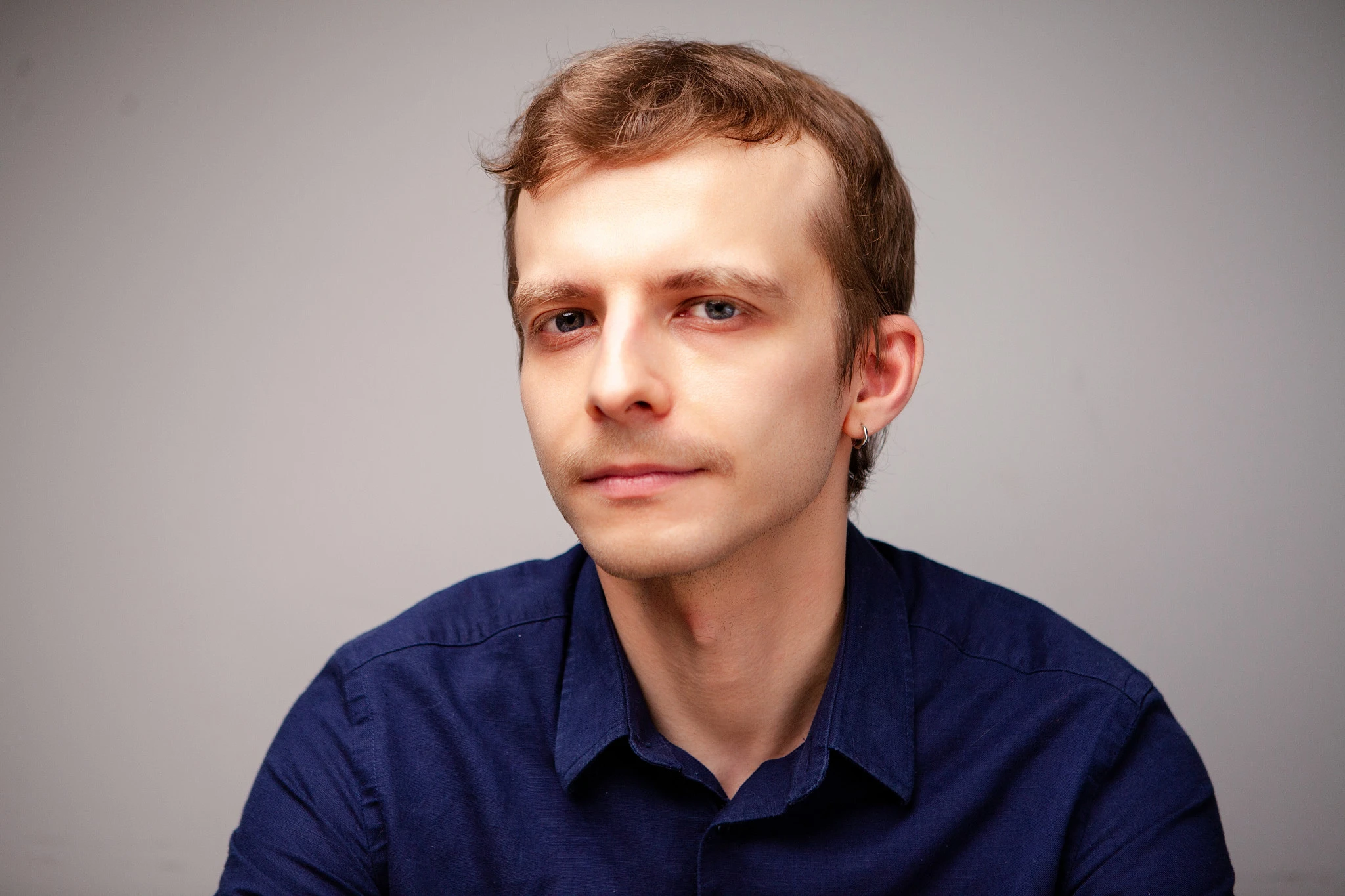 Мужчина в тёмной рубашке на сером фоне слегка повернут в профиль, взгляд сосредоточен в сторону.