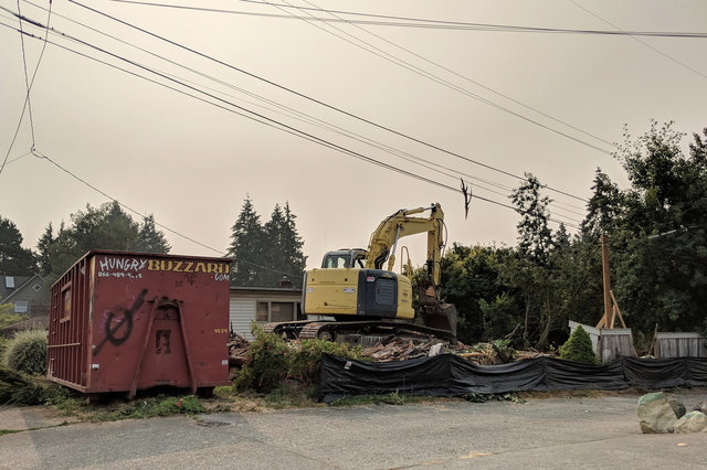 Backhoe clearing a demolished house under wildfire haze