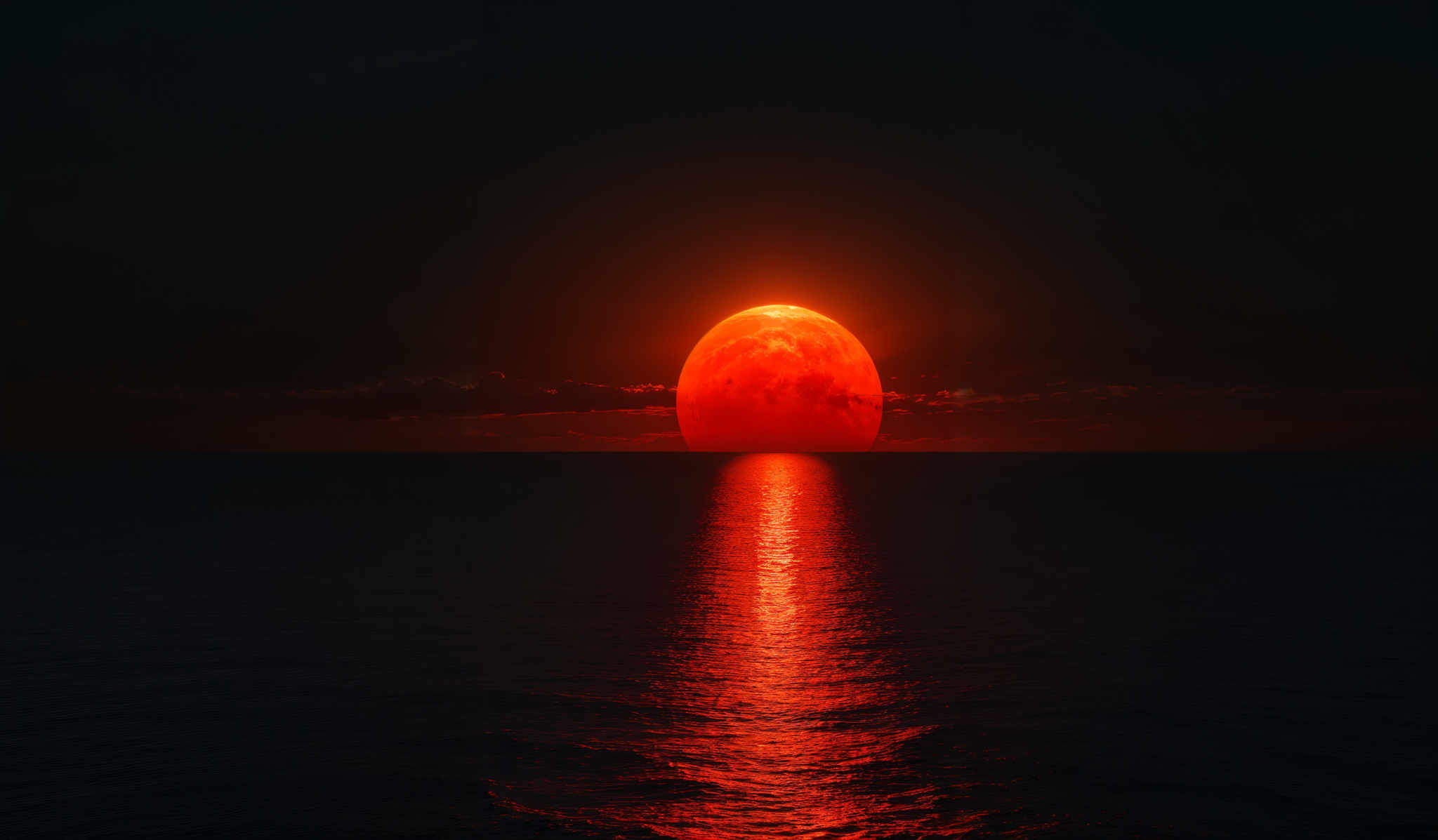 The image showcases a breathtaking view of the ocean during what appears to be either sunrise or sunset. The dominant color is a deep, fiery red, emanating from the large, glowing moon that is partially obscured by a thin layer of clouds. The moon's reflection creates a shimmering pathway on the water's surface, leading the viewer's eye towards the horizon. The vast expanse of the dark ocean contrasts with the intense luminosity of the moon and the subtle hues of the sky, which transition from a deep blue at the top to a lighter, almost golden shade near the horizon, hinting at the presence of the sun just beyond the frame.