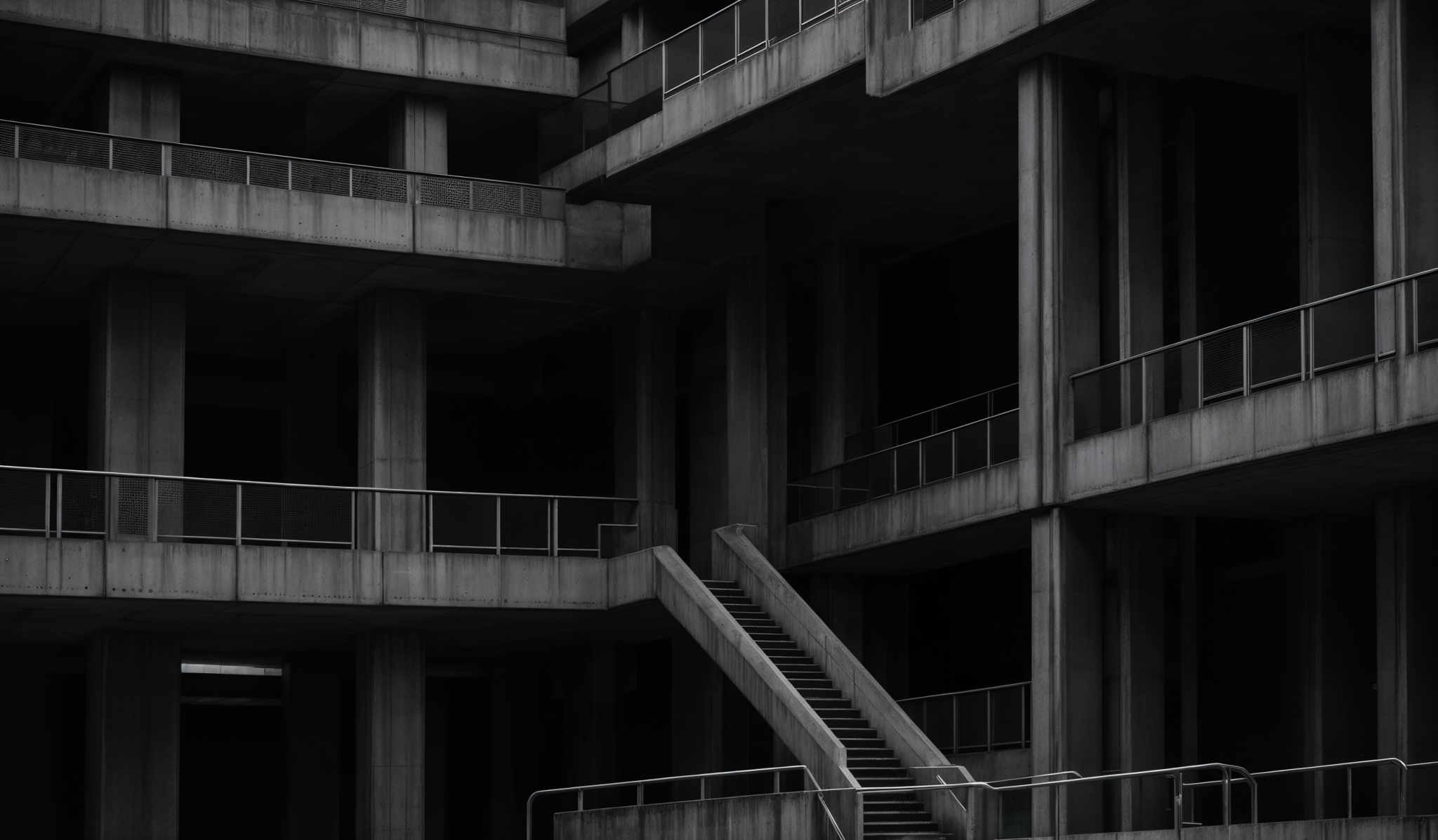 The image showcases a monochromatic, possibly black and white, architectural photograph. It features a multi-story structure with a brutalist design. The predominant colors are shades of gray, emphasizing the raw concrete texture. The structure consists of interconnected platforms, staircases, and railings. The overall shape is geometric, with rectangular and angular forms, and the image captures the intricate details of the architectural elements.