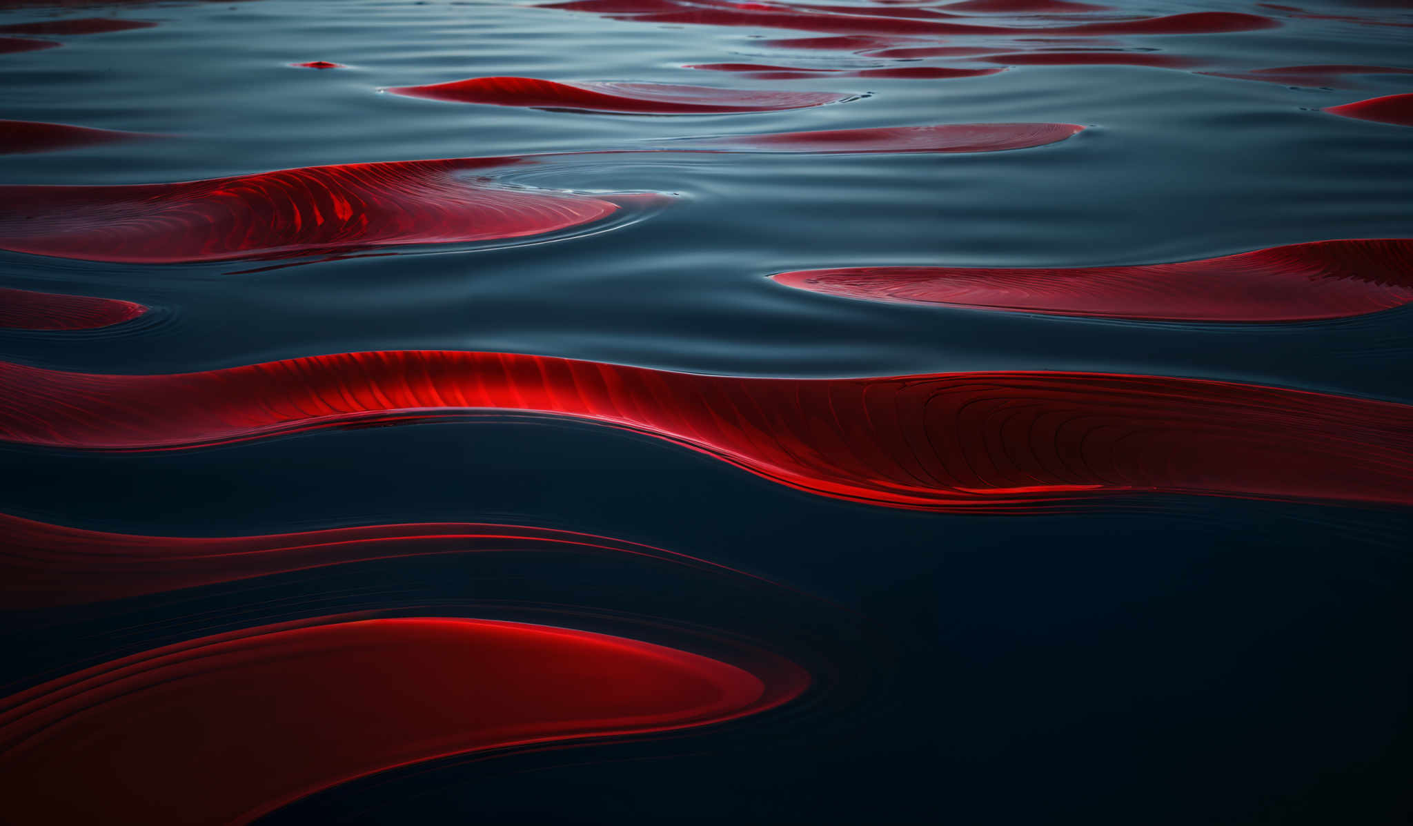 The image showcases a vibrant and intricate pattern of red and black. The red appears to be a fluid or liquid, possibly resembling blood or some other liquid, that is flowing and creating undulating patterns on a darker background. The patterns are reminiscent of waves or ripples, and the fluidity of the red gives it a dynamic and fluid appearance.