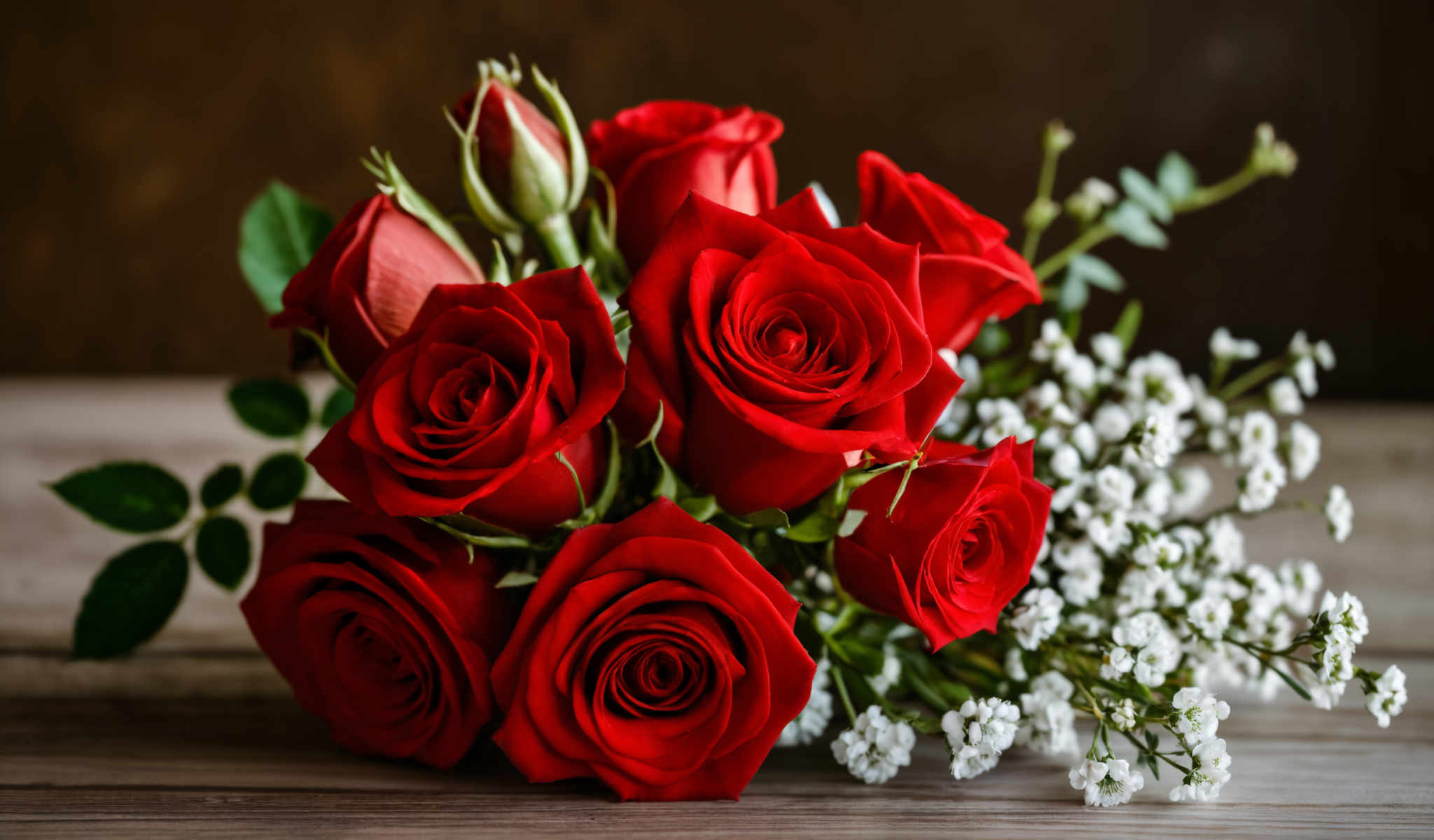 A bouquet of red roses with green stems and white flowers.