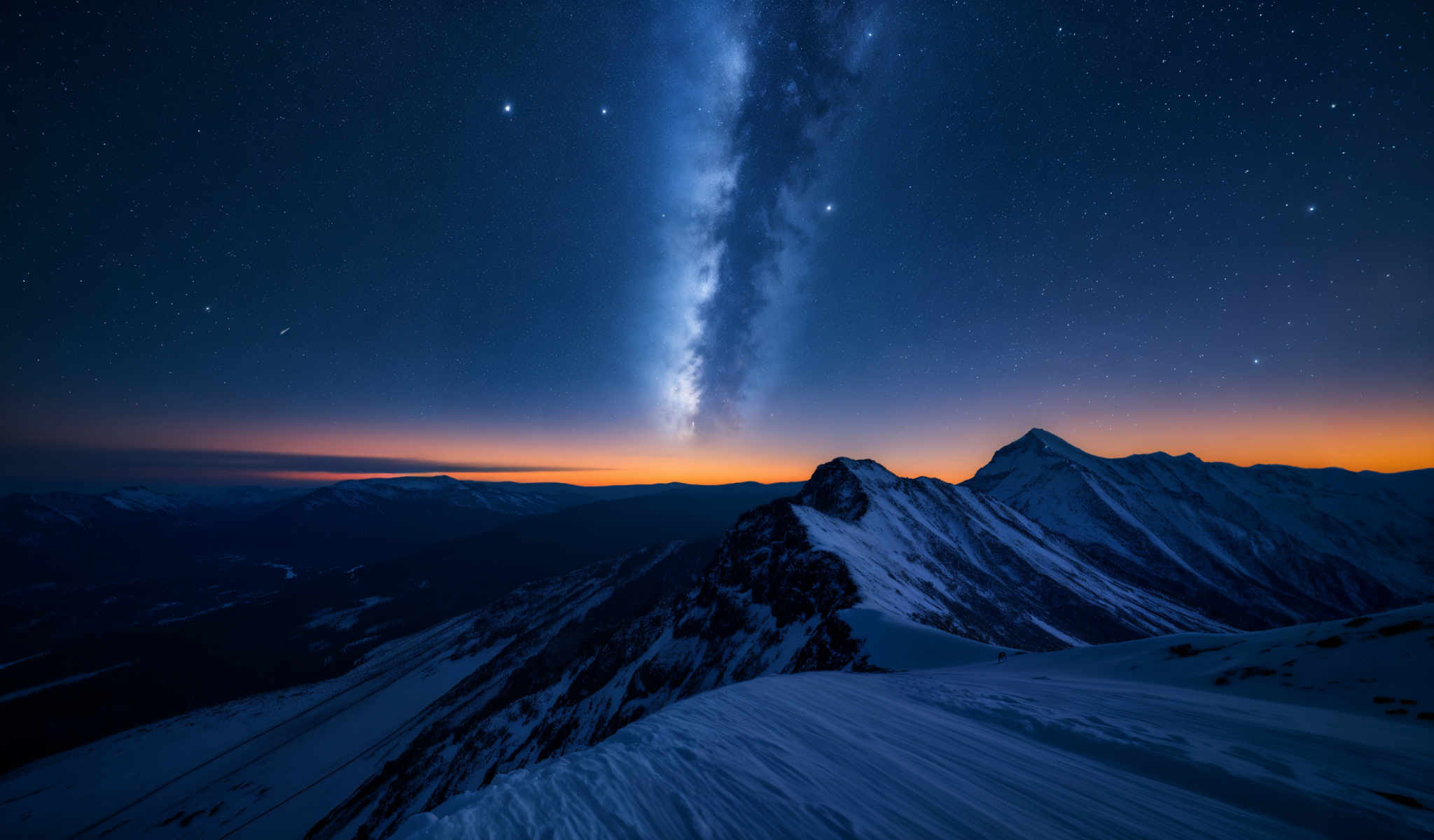 A breathtaking view of a mountain range at sunset. The sky is painted with hues of orange and blue and the mountains are covered in a blanket of snow. The sun is setting behind the mountains casting a warm glow on the scene. The mountains are jagged and rocky adding a sense of ruggedness to the landscape. The image is taken from a high vantage point providing a panoramic view of the mountains and the sky. The colors in the image are vibrant and the lighting is dramatic creating a sense depth and dimension. The overall scene is serene and majestic capturing the beauty of nature in its raw form.