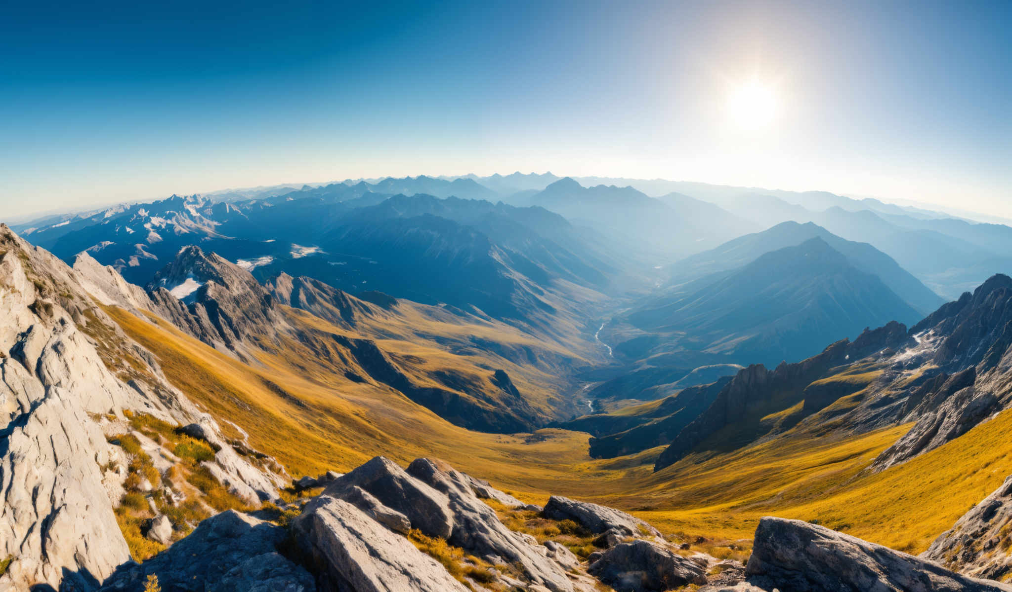 A breathtaking view of a mountain range with a river meandering through it. The mountains are a mix of green and brown indicating a healthy ecosystem. The sky is a clear blue with a few clouds scattered across it. A bright sun is shining in the top right corner of the photo casting a warm glow over the scene. The photo is taken from a high vantage point giving a panoramic view of the landscape. The river appearing as a thin line winds its way through the mountains adding a dynamic element to the otherwise static scene.