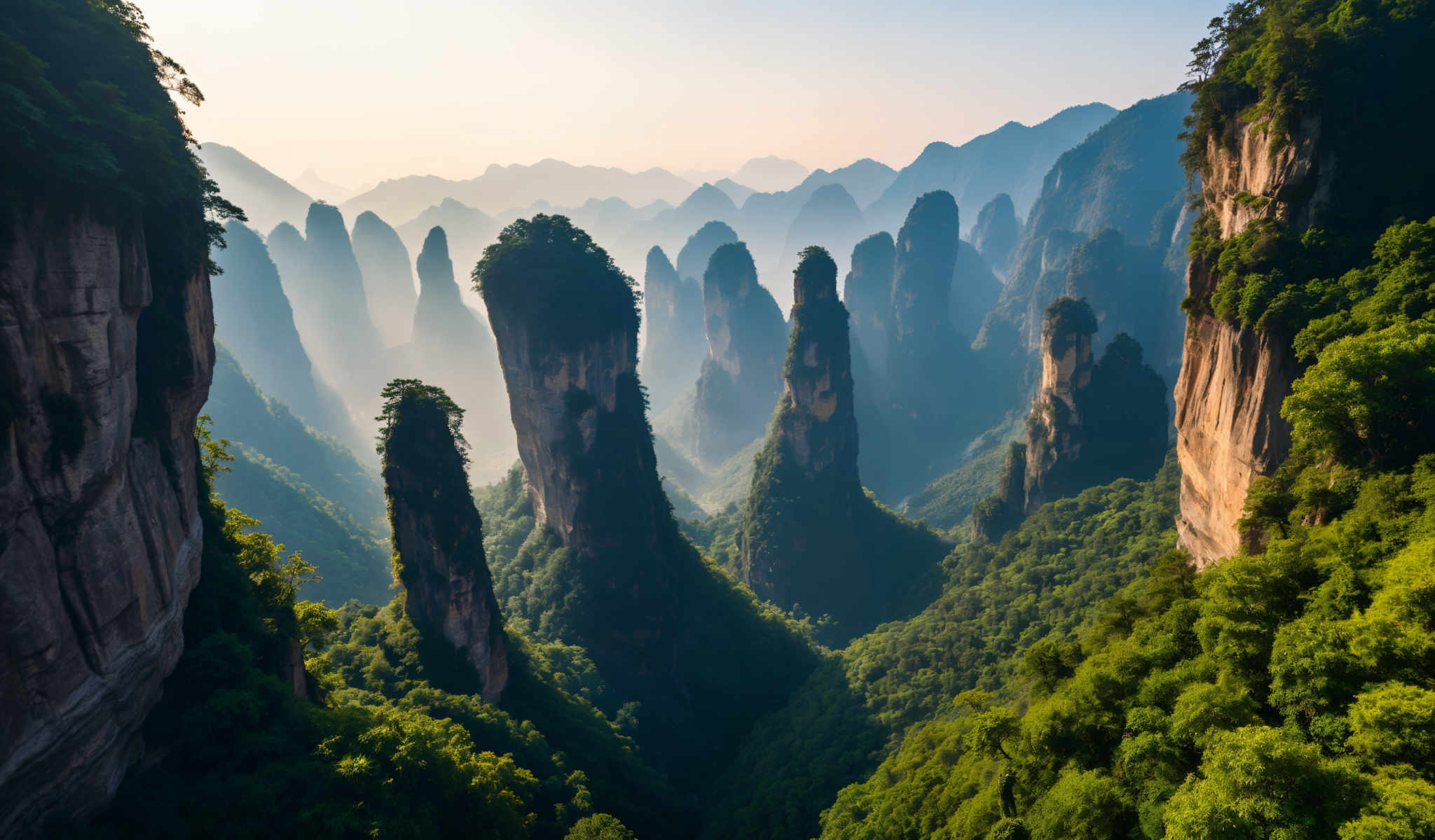 The image captures a breathtaking view of a mountainous landscape. The mountains covered in lush greenery rise majestically from the ground their peaks shrouded in a light mist. The sky above is a clear blue providing a stunning backdrop to the scene. The perspective of the photo is from a high vantage point looking down on the mountains giving a sense of their grandeur and scale. The image is a testament to the beauty of nature and the awe-inspiring power of mountains.